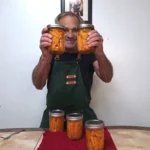 Holding 2 jars of dill pickle carrots with 3 more on the table