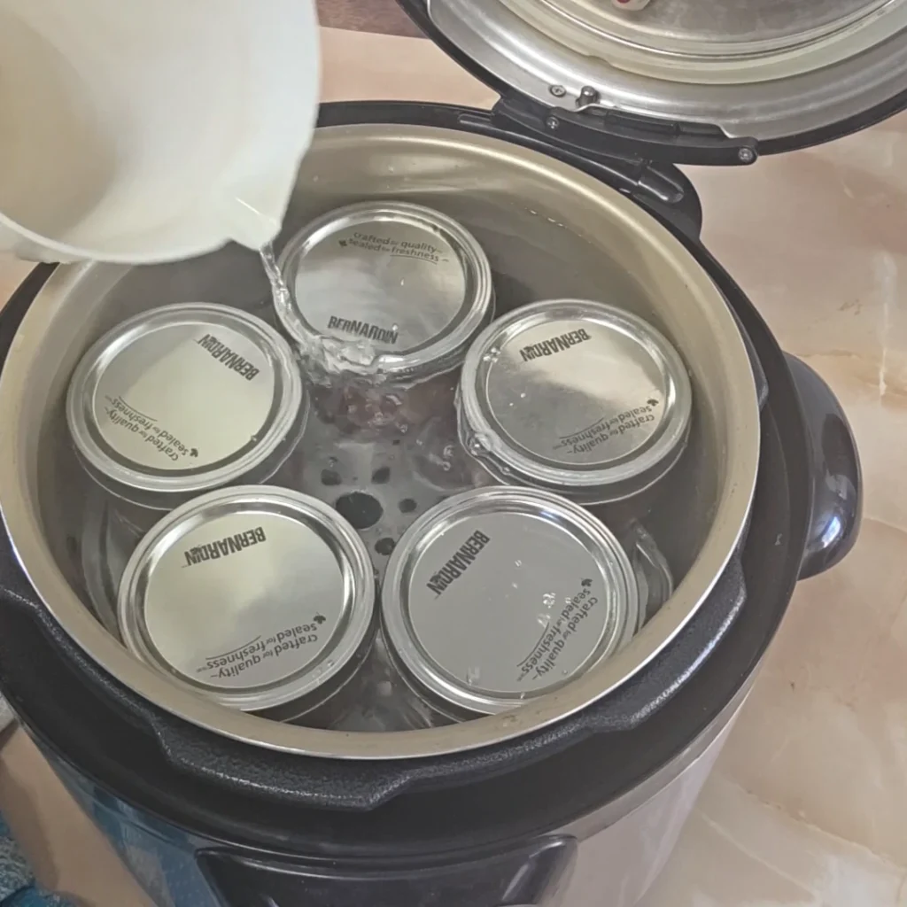 Pouring water into canner filled with jars of BBQ sauce