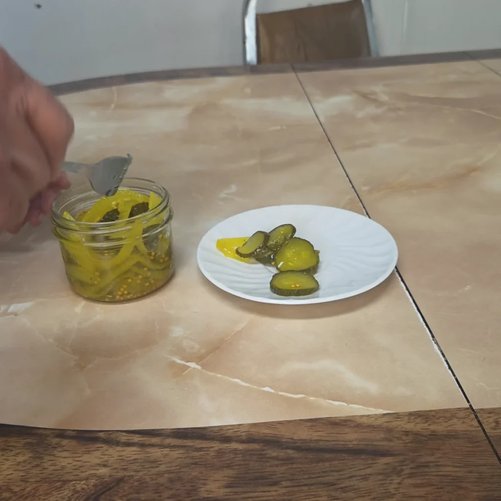 Open jar of pickles with some on a plate